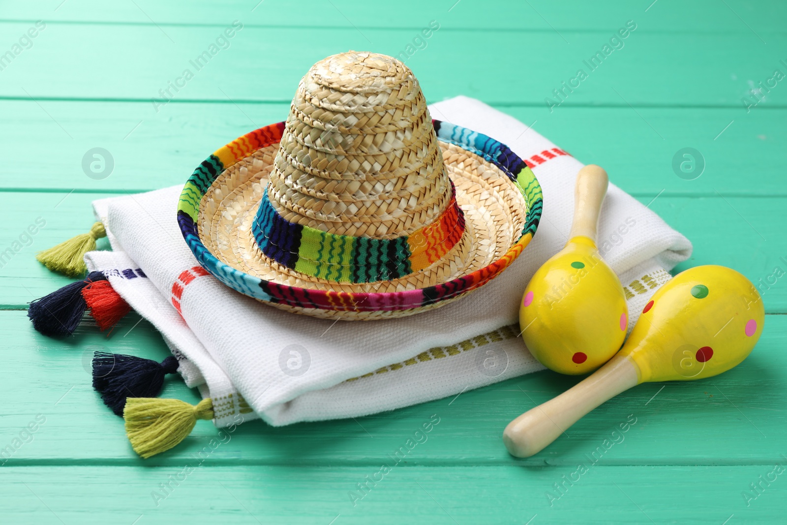 Photo of Mexican sombrero hat, maracas and poncho on turquoise wooden table