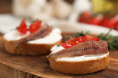 Delicious sandwiches with cream cheese, anchovies and tomatoes on wooden board, closeup. Space for text