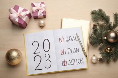 Photo of Flat lay composition of notebook with text 2023 Goal, Plan, Action and festive decor on wooden table. New Year resolutions