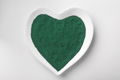 Photo of Heart shaped plate with spirulina algae powder on white background, top view