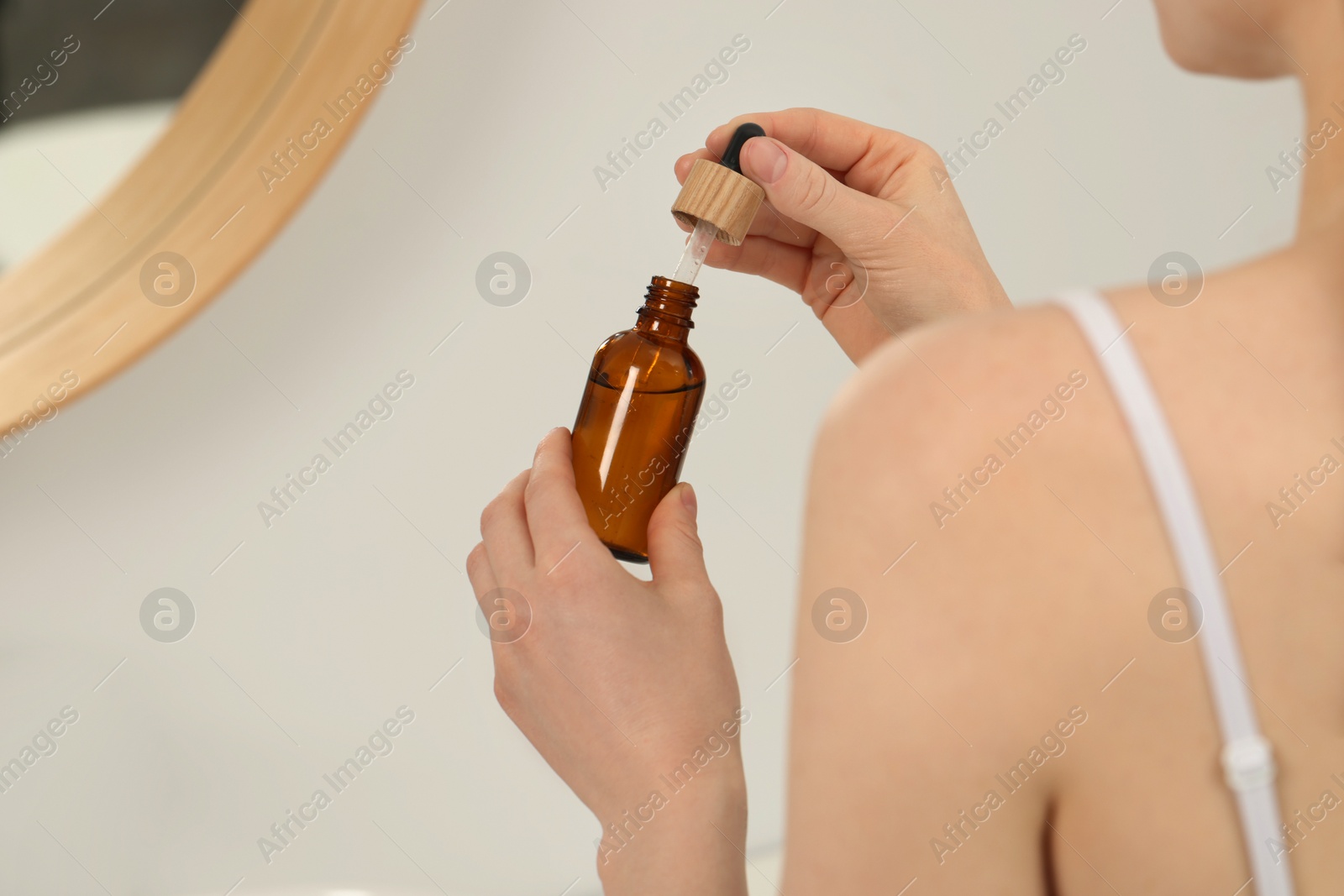 Photo of Woman with bottle of essential oil on blurred background, closeup