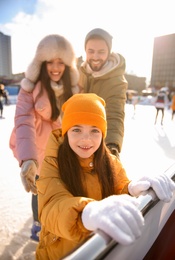 Photo of Cute little girl with her parents at outdoor ice skating rink