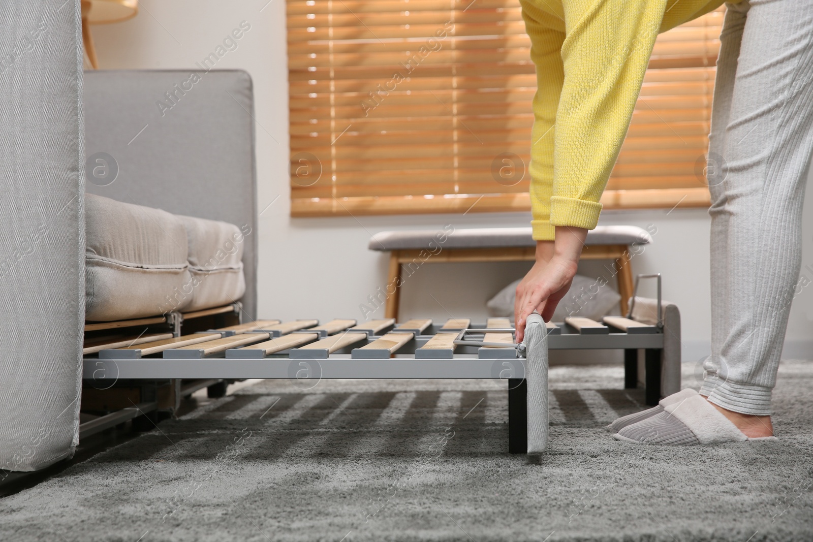 Photo of Young woman unfolding sofa into a bed in room, closeup. Modern interior