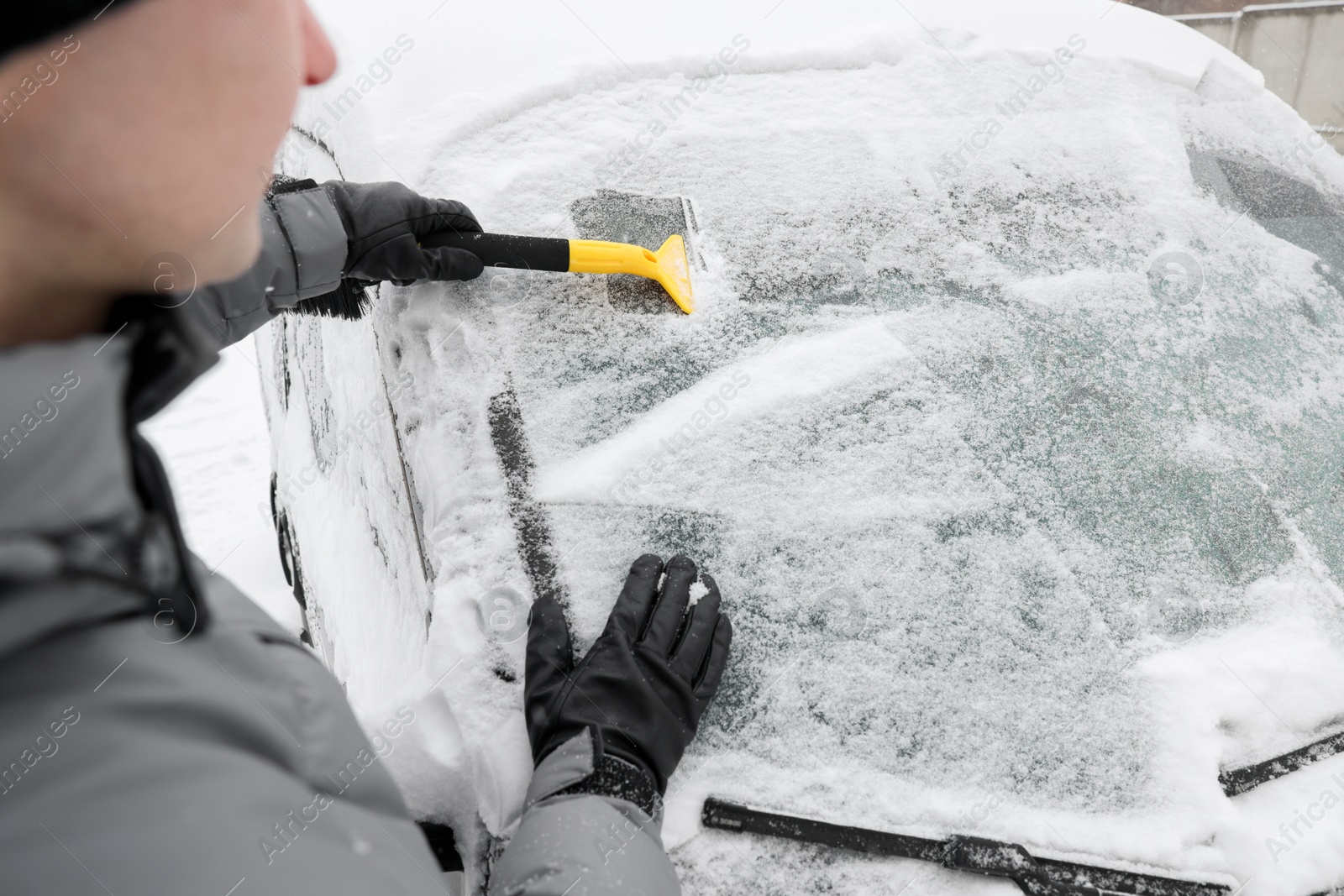 Photo of Man cleaning snow from car windshield outdoors, closeup