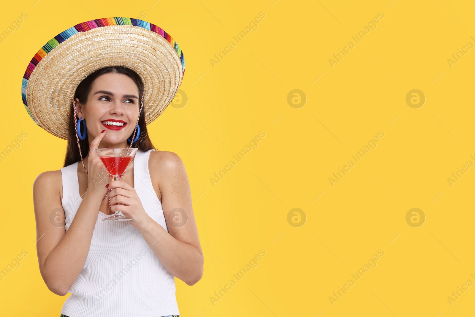 Photo of Young woman in Mexican sombrero hat with cocktail on yellow background. Space for text