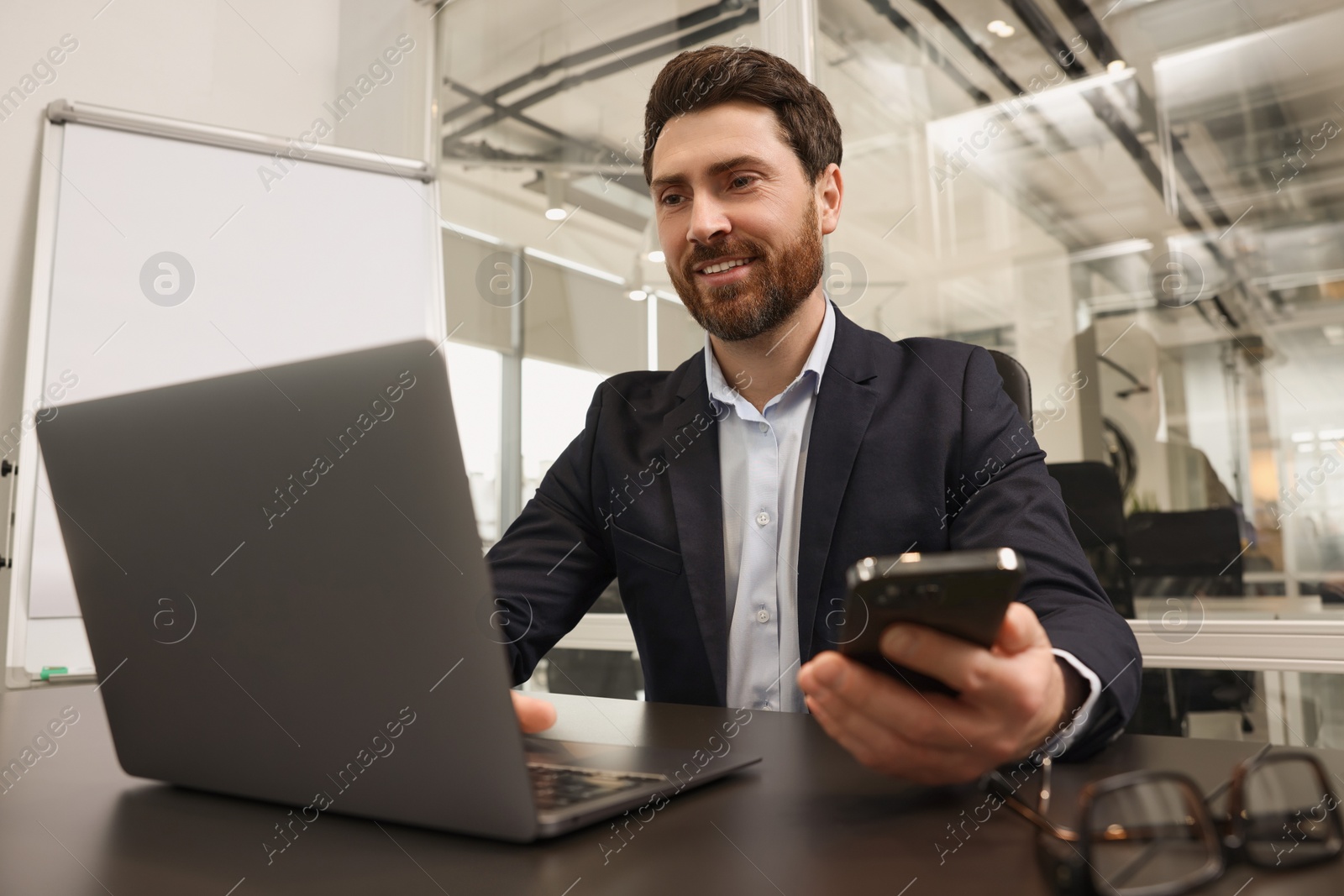 Photo of Man with phone working on laptop at black desk in office