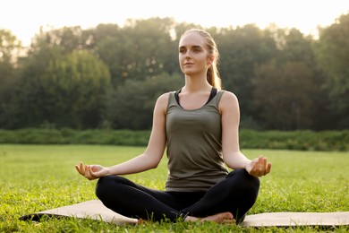 Photo of Beautiful woman practicing yoga on mat outdoors. Lotus pose