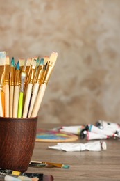 Photo of Different paintbrushes in holder on wooden table, closeup. Space for text