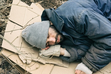 Poor homeless man lying on cardboard outdoors