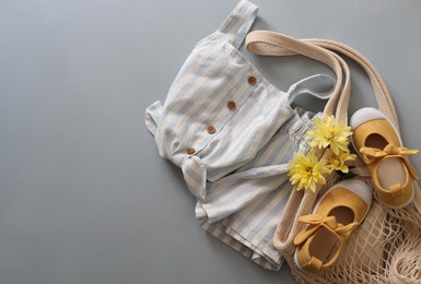 Photo of Stylish child clothes, shoes, flowers and mesh bag on grey background, flat lay. Space for text