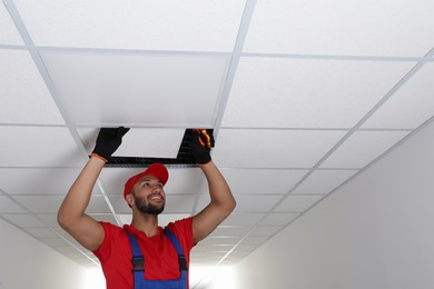 Photo of Electrician with pliers repairing ceiling light indoors, space for text