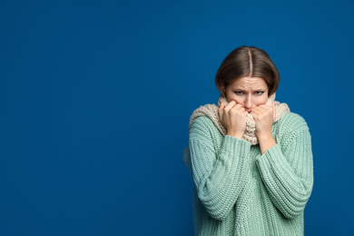 Young woman wearing scarf suffering from fever on blue background, space for text. Cold symptoms