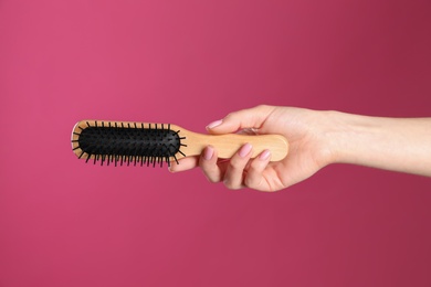 Photo of Woman holding wooden hair brush against crimson background, closeup