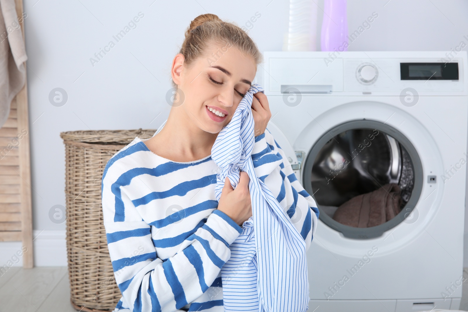 Photo of Young woman with clean clothes in bathroom. Laundry day