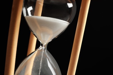 Hourglass with flowing sand on black background, closeup. Time management