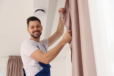 Worker in uniform hanging window curtain indoors