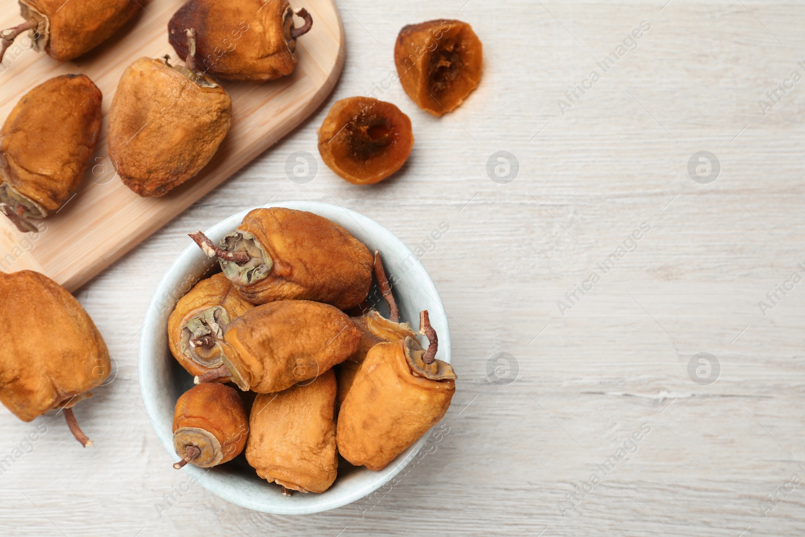 Photo of Bowl with tasty dried persimmon fruits on wooden table, flat lay. Space for text