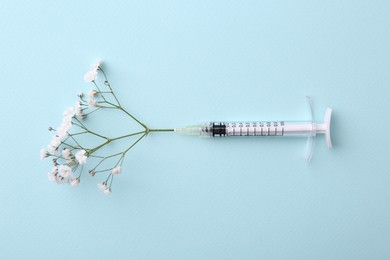Photo of Cosmetology. Medical syringe and gypsophila on light blue background, top view