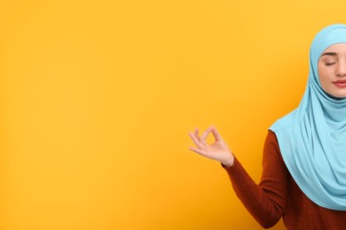 Muslim woman in hijab meditating on orange background, space for text