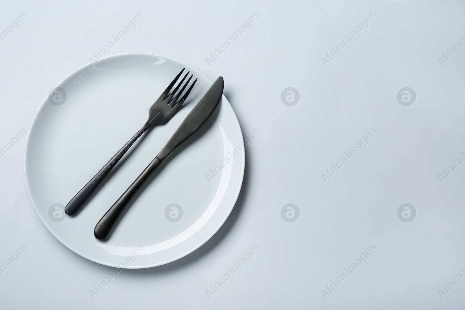 Photo of Clean white plate with cutlery on light grey background, top view. Space for text