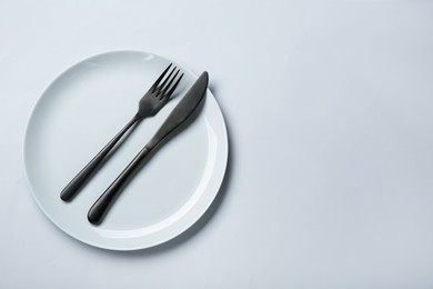 Clean white plate with cutlery on light grey background, top view. Space for text