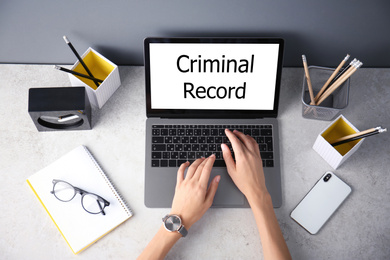 Woman using laptop with words CRIMINAL RECORD at table, top view