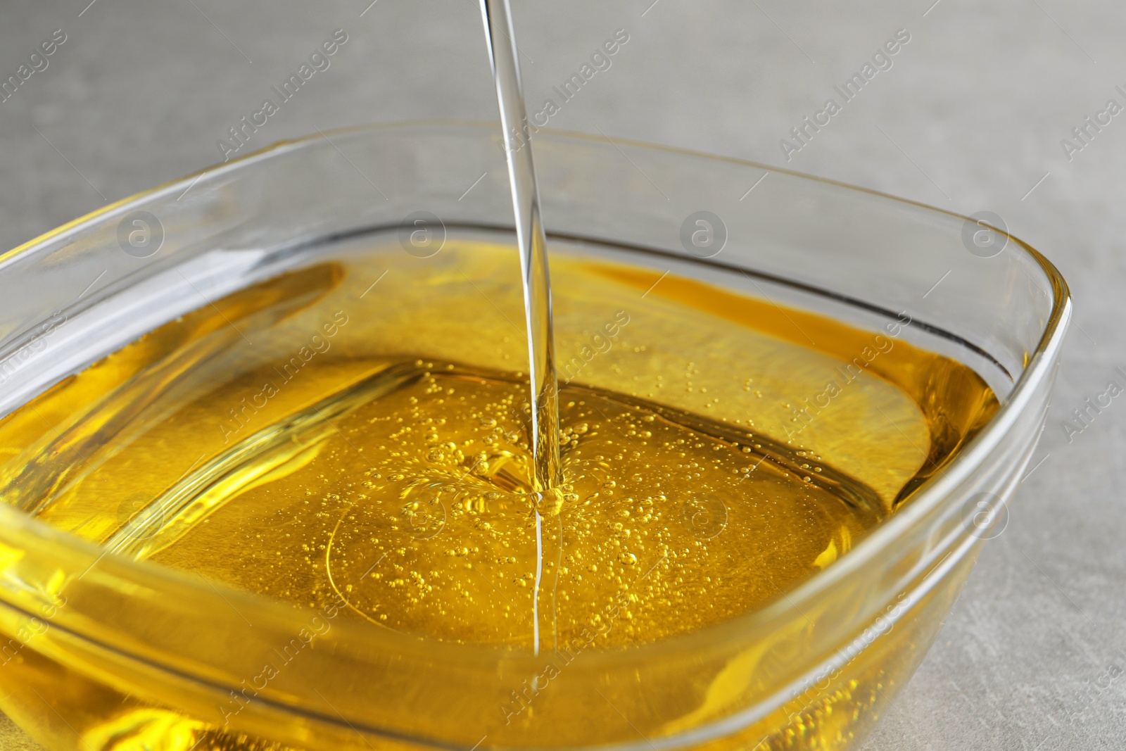 Photo of Pouring cooking oil into bowl on light background, closeup