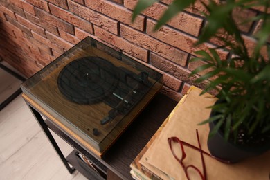 Stylish turntable and vinyl records on shelving unit near red brick wall indoors