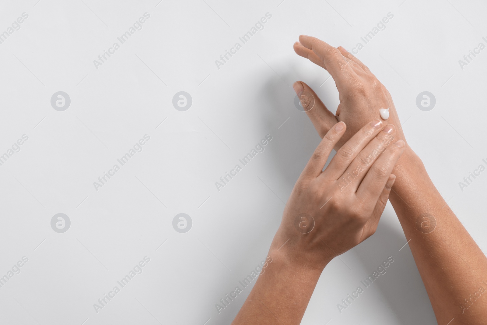 Photo of Woman applying cosmetic cream onto hand on white background, top view. Space for text