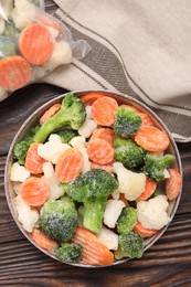 Mix of different frozen vegetables in bowl on wooden table, top view
