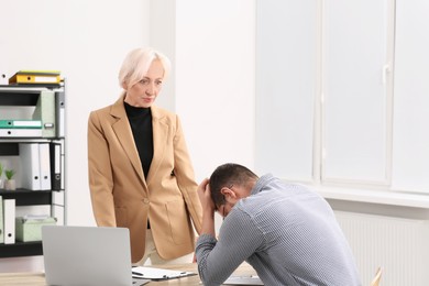 Photo of Boss and stressed employee discussing work issues at wooden table in office
