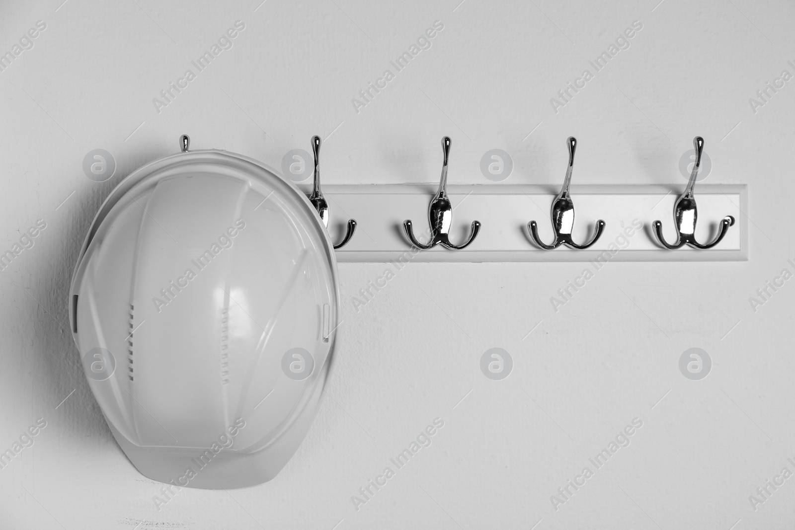 Photo of Hard hat hanging on white wall. Safety equipment