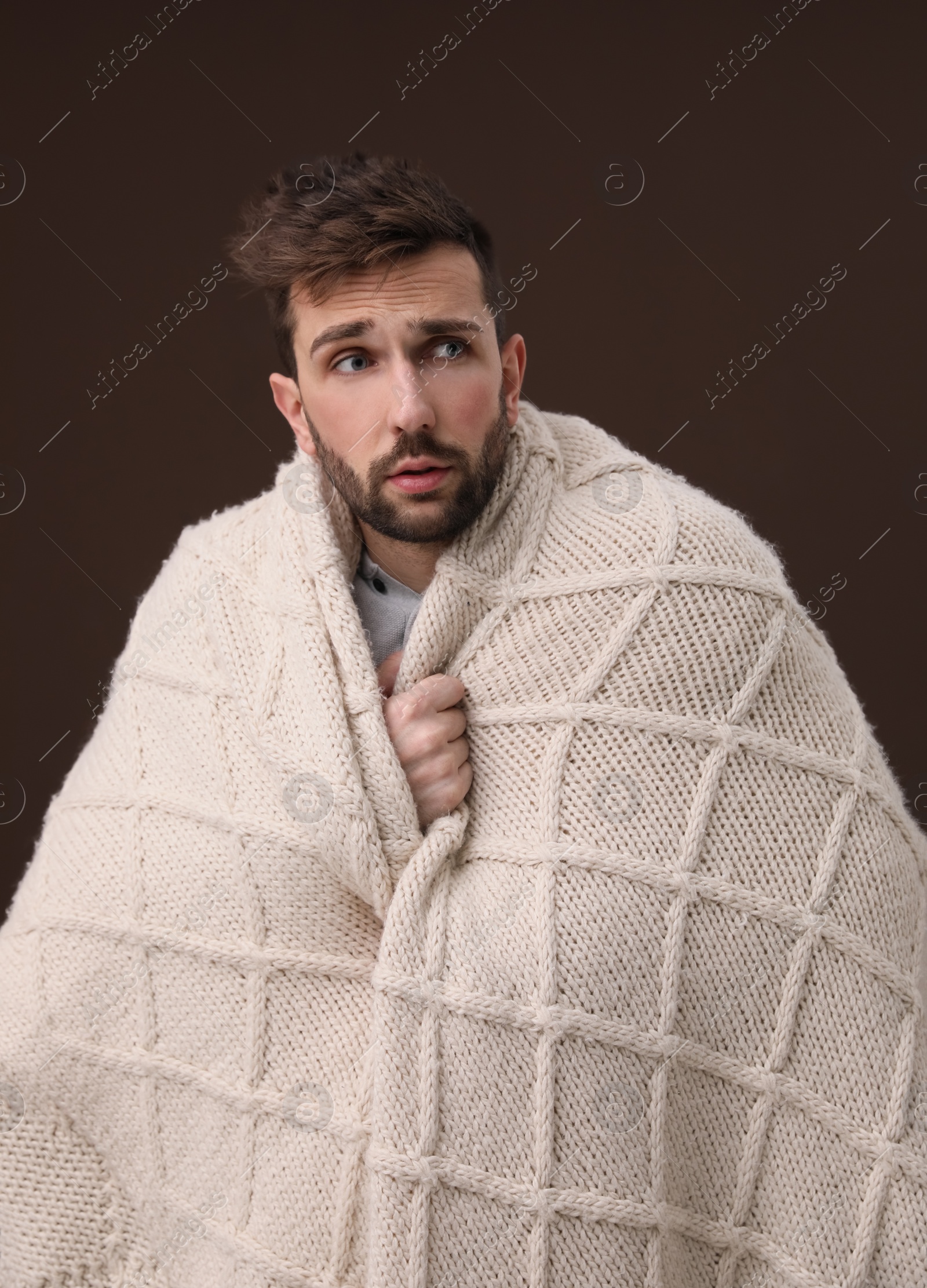 Photo of Man wrapped in blanket suffering from fever on brown background. Cold symptoms