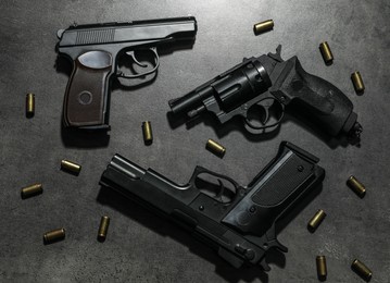 Photo of Different guns and bullets on grey table, flat lay