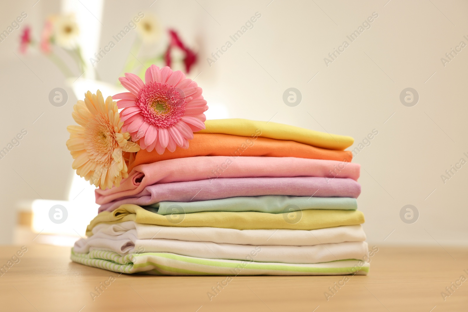 Photo of Stack of clean clothes and flowers on wooden table