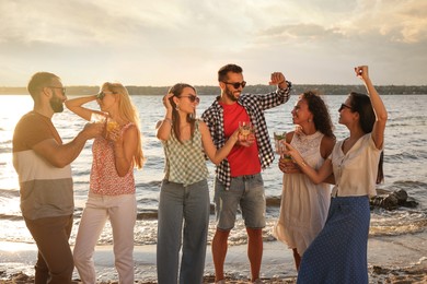 Photo of Group of friends with drinks having fun near river at summer party