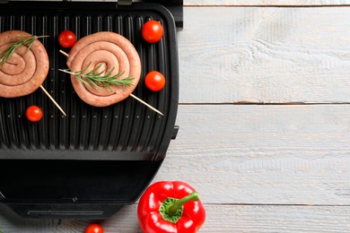 Photo of Electric grill with homemade sausages, rosemary and vegetables on rustic wooden table, flat lay. Space for text