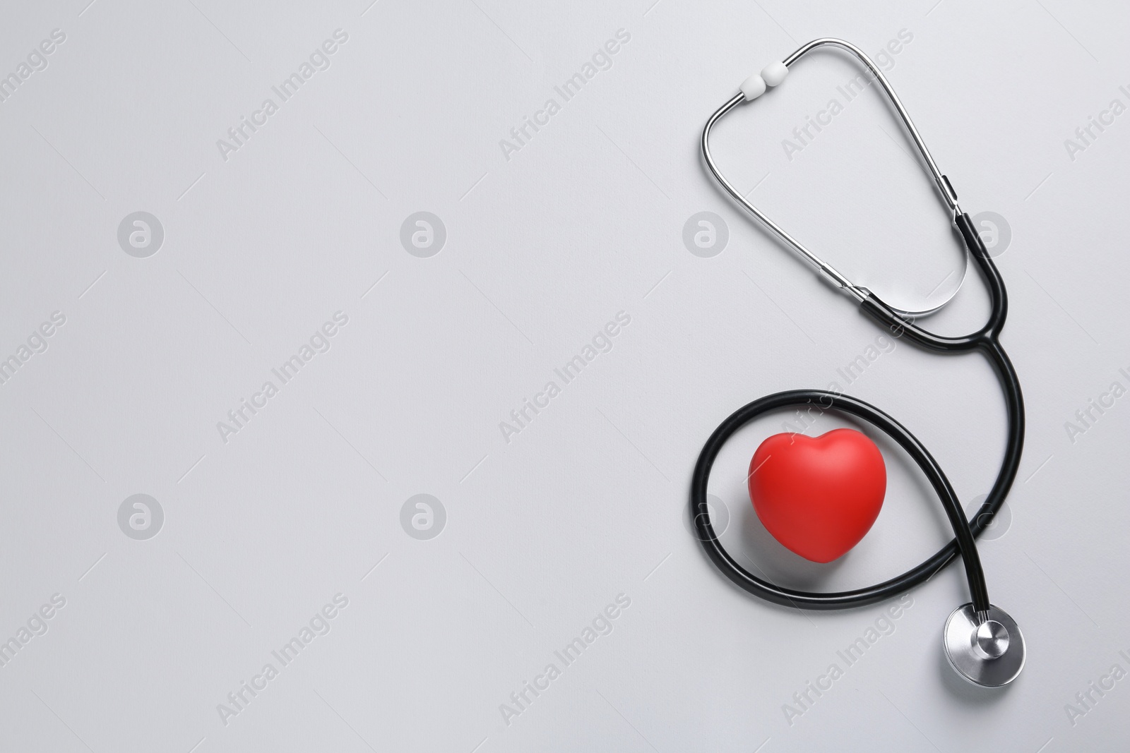 Photo of Stethoscope, red decorative heart on grey background, flat lay with space for text. Cardiology concept