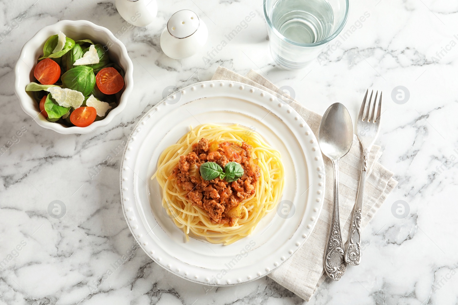 Photo of Delicious pasta bolognese served with vegetable salad on marble background, top view