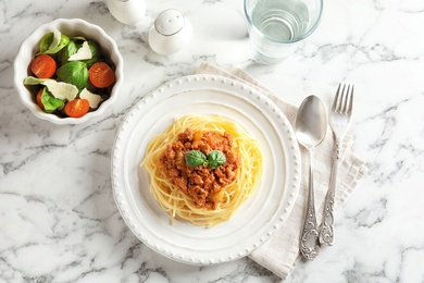 Delicious pasta bolognese served with vegetable salad on marble background, top view