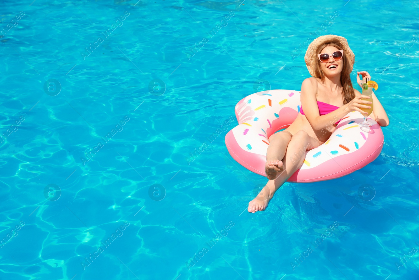 Photo of Young woman with cocktail in pool on sunny day