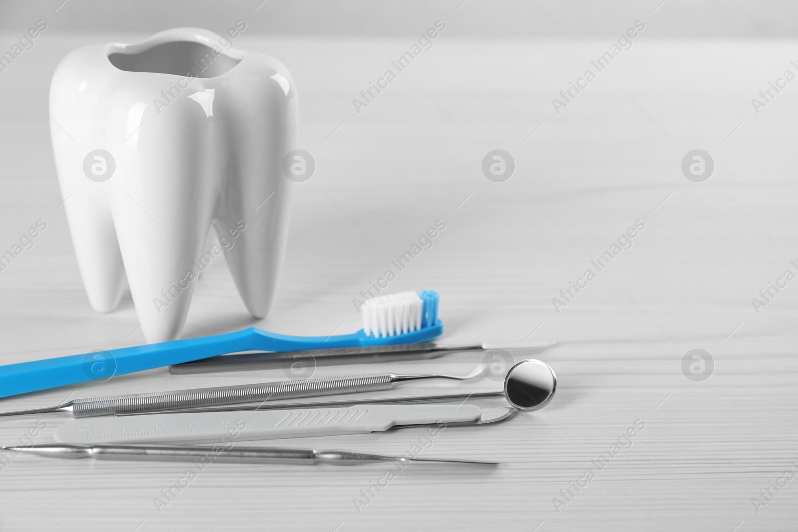 Photo of Tooth shaped holder with set of dentist's tools and brush on wooden table. Space for text