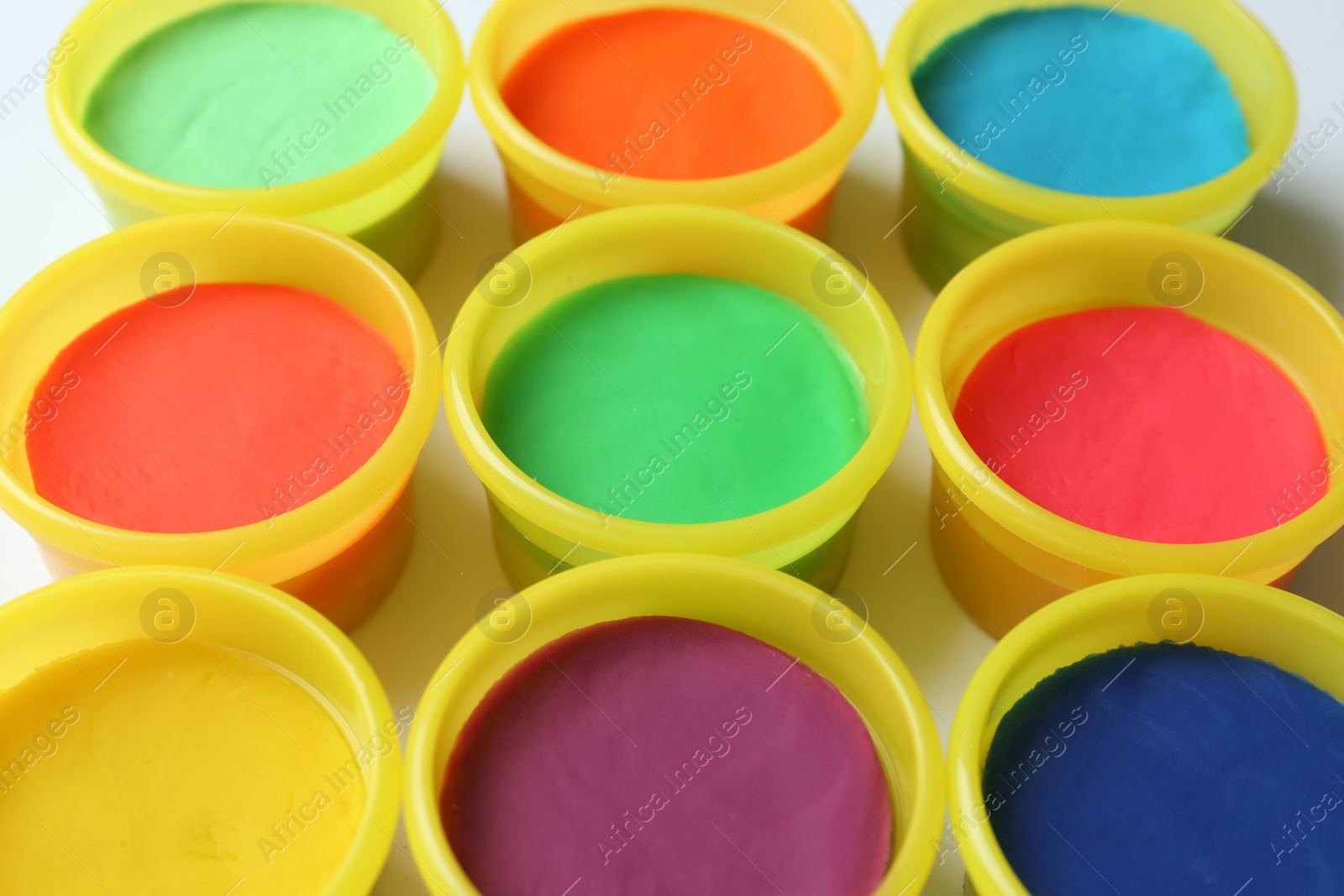 Photo of Plastic containers with colorful play dough on white background, closeup