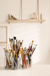 Photo of Different paintbrushes on white table indoors. Artist's workplace
