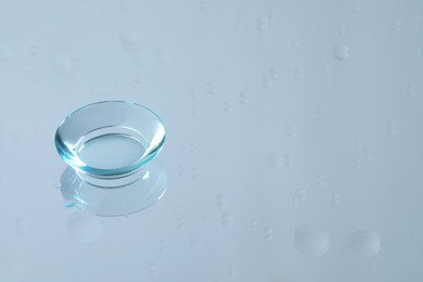 Photo of Contact lens on wet light blue reflective surface. Space for text