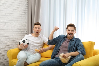 Photo of Men with snacks and ball watching soccer match on TV in living room