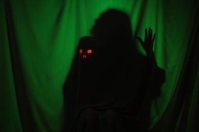 Silhouette of creepy ghost with skull behind dark green cloth