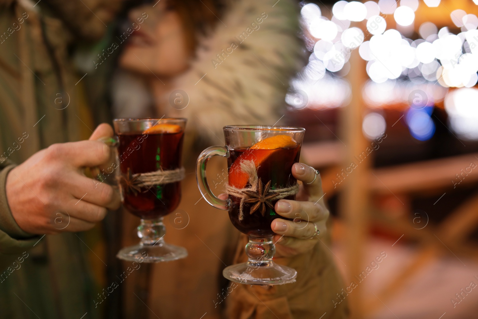 Photo of Young couple with glass cups of mulled wine at winter fair, closeup. Space for text