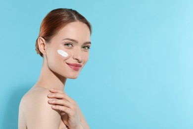 Beautiful young woman with sun protection cream on her face against light blue background, space for text