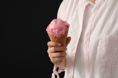 Photo of Woman holding pink ice cream in wafer cone on black background, closeup. Space for text